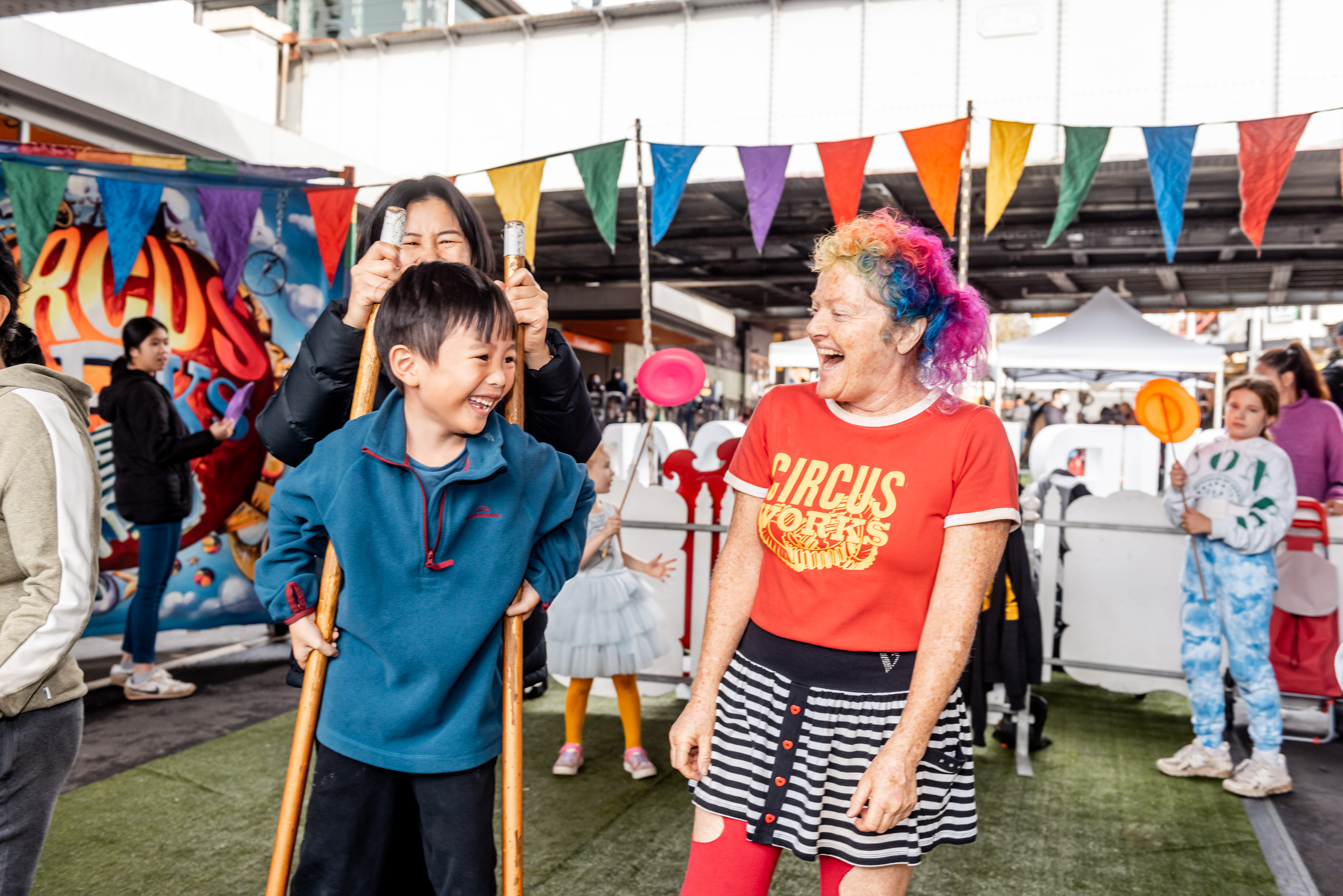 A child on stilts smiling with a circus performer laughing next to him