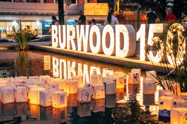 lanterns floating on pond with large light up 'Burwood 150' sign behind them