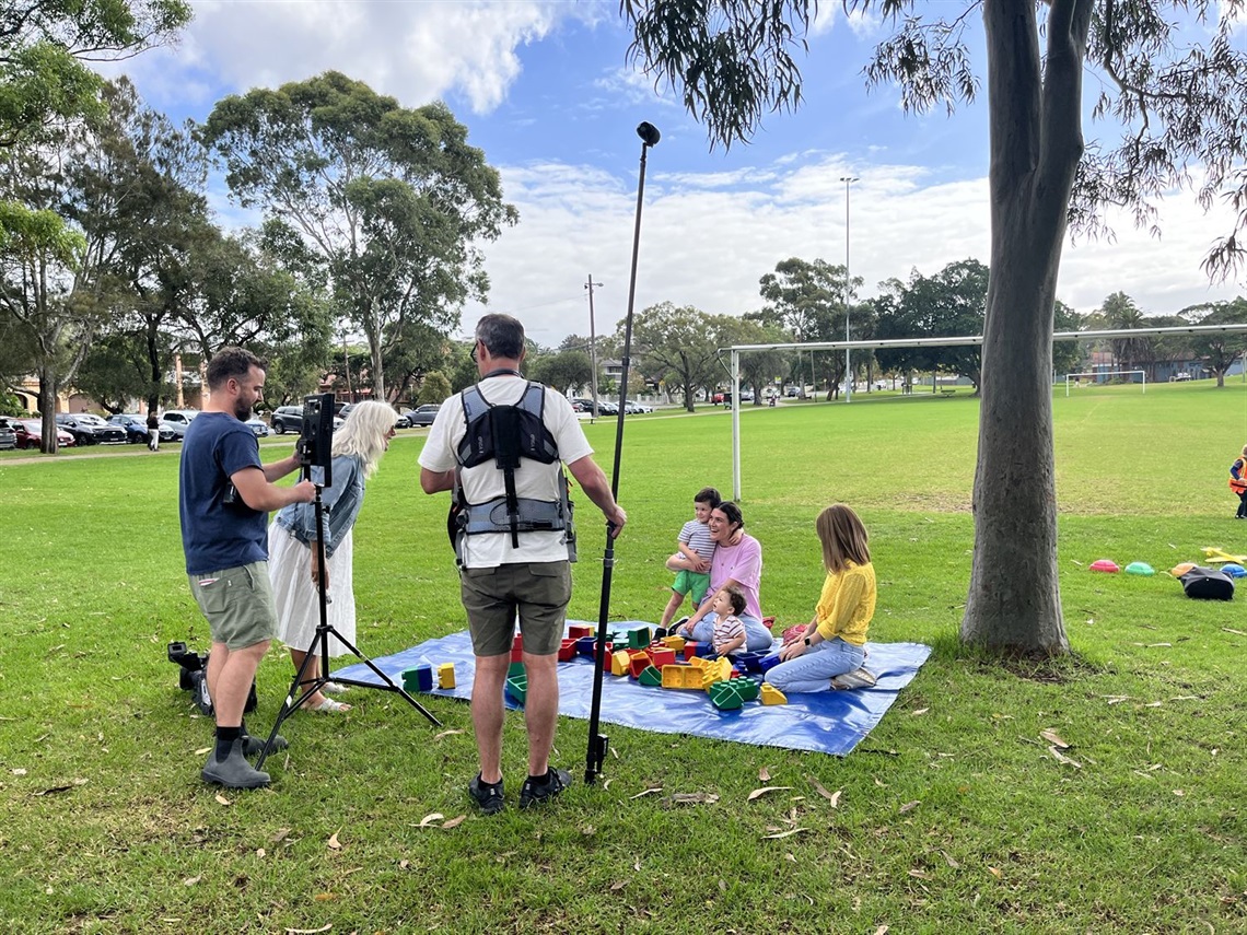 A film crew in a park on a sunny day interviewing a mother and her son