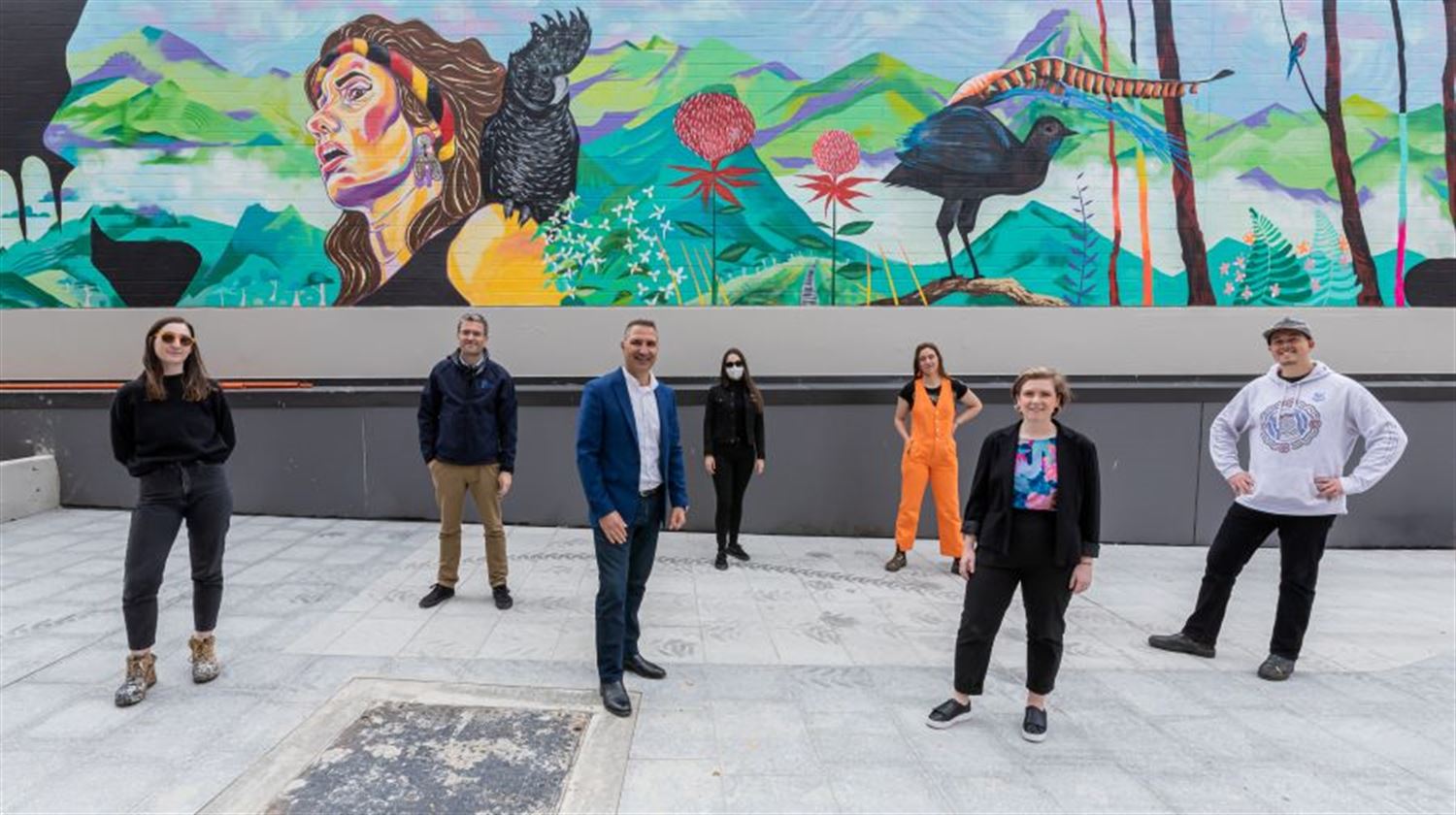 the mayor and artists stood in front of the bright wall mural
